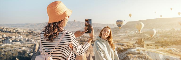 Junge Frau fotografiert ihre Freundin vor aufsteigenden Heißluftballons